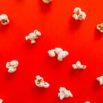 Scattered popcorn on a bold red surface in a flat lay style, perfect for snack-themed concepts.